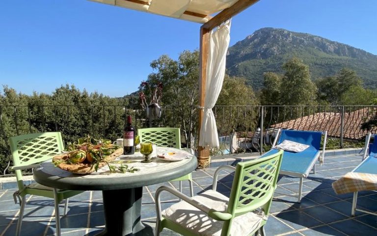 Terrazza con sedie, tavolo con vino e cibo, due sdraio e vista sui monti dell'Ogliastra, Sardegna