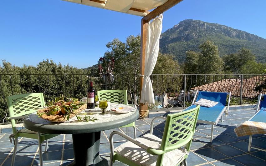 Terrazza con sedie, tavolo con vino e cibo, due sdraio e vista sui monti dell'Ogliastra, Sardegna
